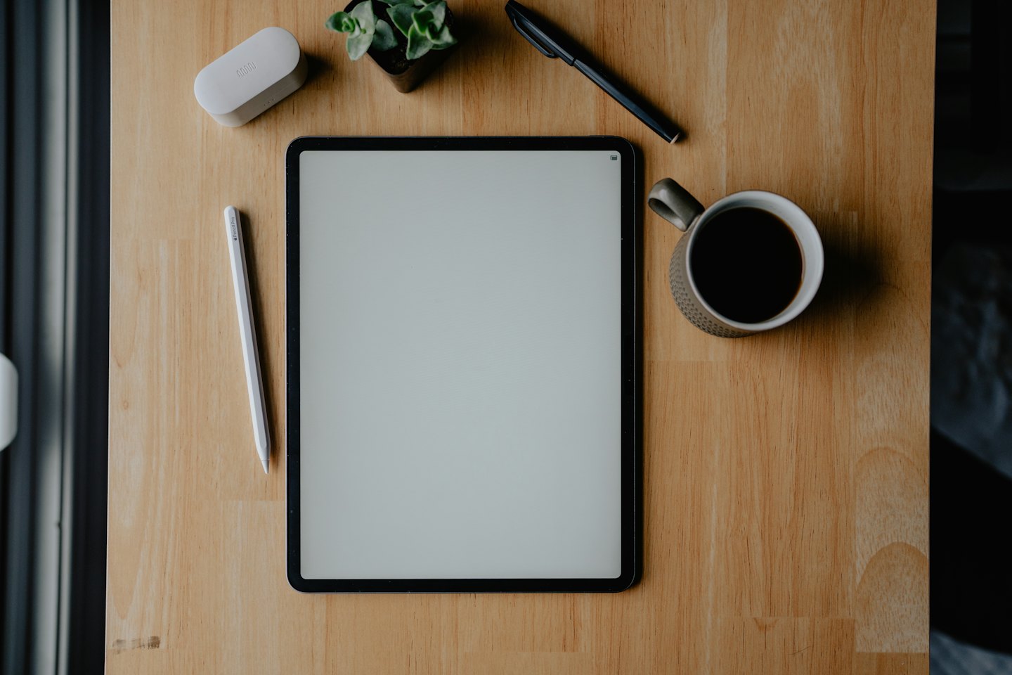 Tablet a kancelárske potreby na drevenom stole.